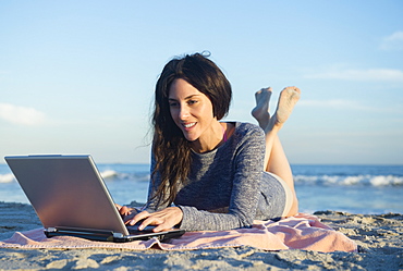 Woman using laptop on beach, Rockaway Beach, New York