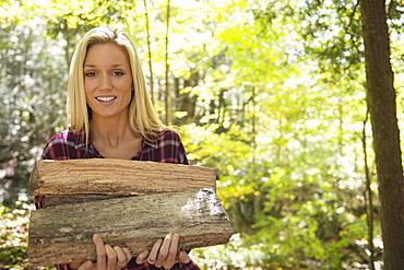 Portrait of woman holding logs in forest, Newtown, Connecticut