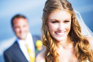 Portrait of smiling bride, groom in background