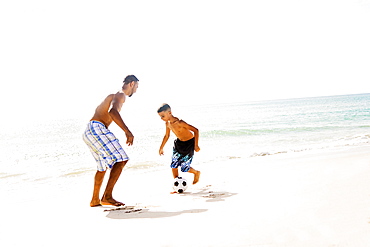 Father and son (10-11) playing soccer on beach