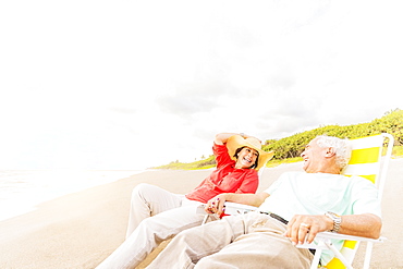 View of couple sitting in lounge chairs on beach and laughing, Jupiter, Florida
