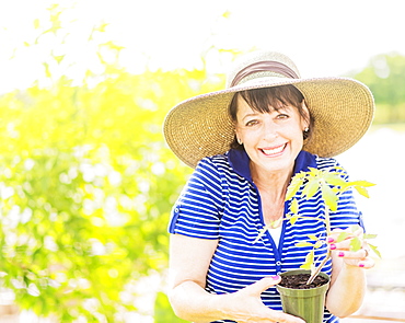 Portrait of smiling woman holding potted plant in garden