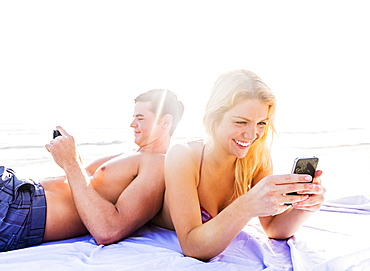 Portrait of young couple relaxing on beach, using smart phones, Jupiter, Florida