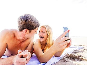 Portrait of young couple lying on blanket on beach, using smart phone, Jupiter, Florida