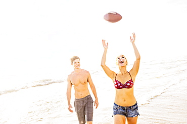 Young woman catching football on beach, Jupiter, Florida