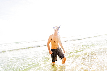 Portrait of young man walking in surf wearing scuba mask and snorkel, Jupiter, Florida