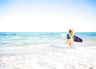 Young woman running in surf into sea carrying surfboard, Jupiter, Florida