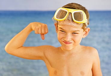 Boy (10-11) wearing swimming goggles flexing muscles