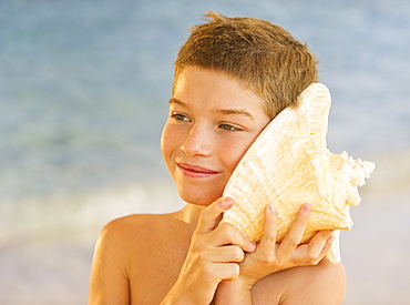 Boy (10-11) listening to sea shell on beach