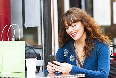 Woman sitting in sidewalk cafe and texting on mobile phone