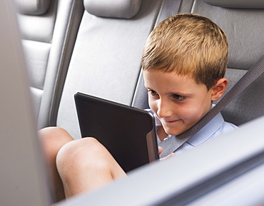 Boy (6-7) using digital tablet while sitting in car