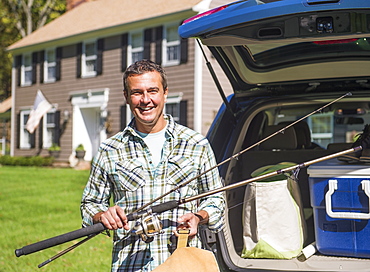 Portrait of man holding fishing rods in front of packed car, Mendham, New Jersey