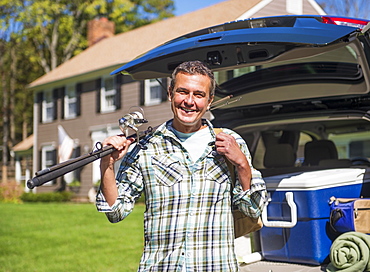 Portrait of man holding fishing rods in front of packed car, Mendham, New Jersey