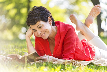 Mature woman lying on grass and reading book