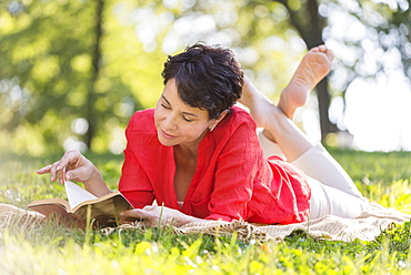 Mature woman lying on grass and reading book