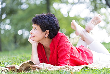 Mature woman lying on grass and reading book