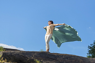 Mature woman standing on rock with arms raised