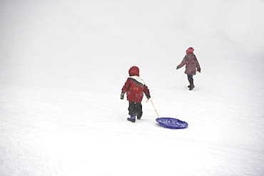 Kids pulling sled up snowy hill