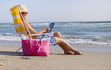 Woman sitting on deckchair and using laptop, Palm Beach, Florida