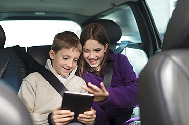 Boy and girl (8-9, 10-11) using digital tablet in car