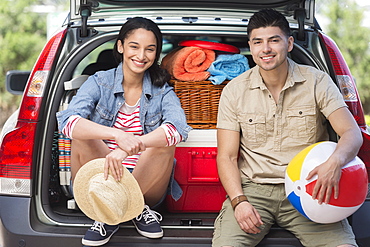 Portrait of young couple sitting in open car trunk