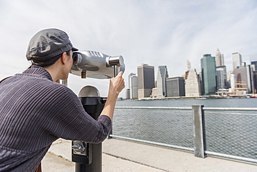 Woman watching cityscape through coin-operated binoculars, Brooklyn, New York