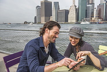 Happy couple sitting and using tablet pc with cityscape in background, Brooklyn, New York