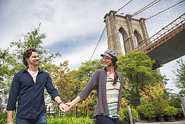 Happy couple holding hands and walking with Brooklyn Bridge in background, Brooklyn, New York