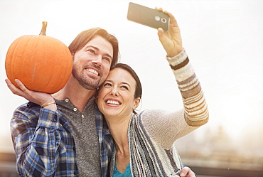 Couple taking selfie with mobile phone, man holding pumpkin