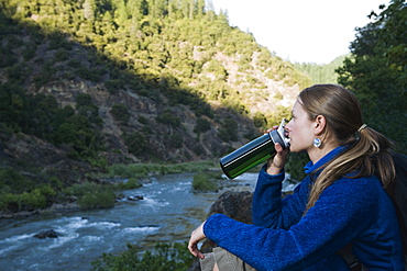 Young woman drinking water on river overlook