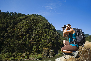 Hiker looking through binoculars on river overlook