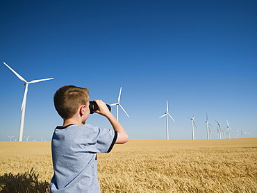 Boy on wind farm looking through binoculars