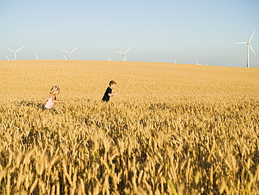 Children running through tall wheat field on wind farm