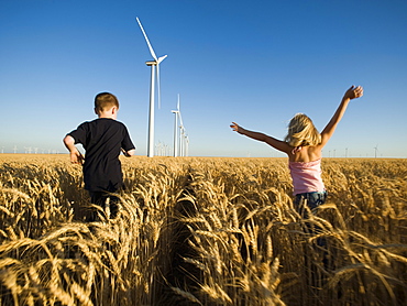 Children running through tall wheat field on wind farm