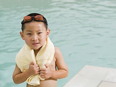 Boy wrapped in towel posing in front of swimming pool