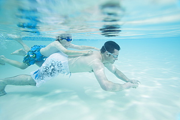 Boy swimming on fatherâ€™s back underwater