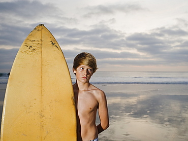 Boy standing beside surfboard