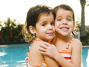 Sister embracing beside pool