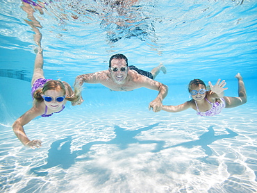 Father with two daughters (6-7,8-9) swimming underwater