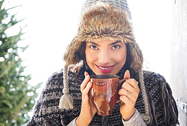 Portrait of young woman wearing winter hat, holding mug