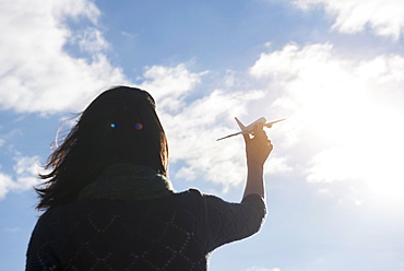 Rear view of young woman holding model airplane against sky