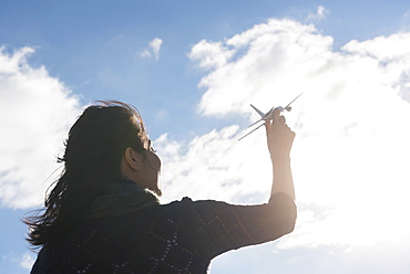 Young woman holding model airplane against cloudy sky