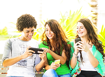 Group of friends (14-15) sitting on bench and texting, Jupiter, Florida