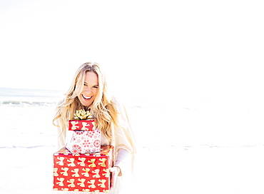 Portrait of smiling woman holding presents on beach