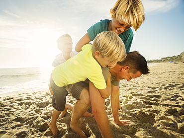 Father playing with his sons (6-7, 10-11, 14-15) on beach, Laguna Beach, California