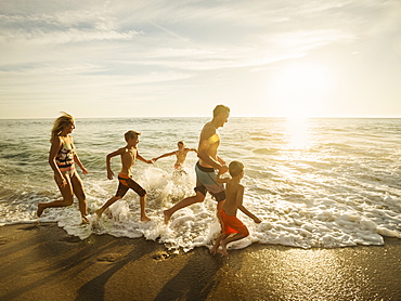 Family with three children (6-7, 10-11, 14-15) running on beach, Laguna Beach, California