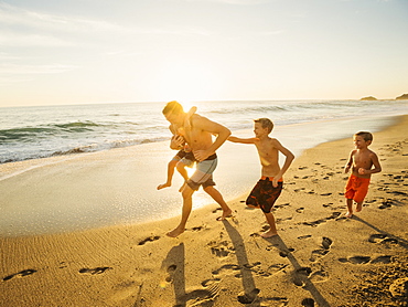 Father playing football on beach with his three sons (6-7, 10-11, 14-15), Laguna Beach, California