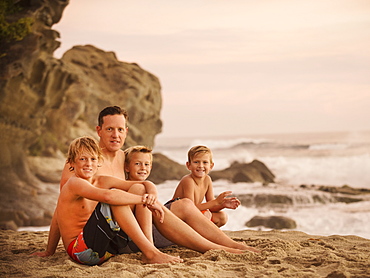 Son with three sons (6-7, 10-11, 14-15) sitting on beach, Laguna Beach, California