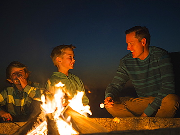 Man talking with his sons (10-11, 14-15) by campfire, Laguna Beach, California