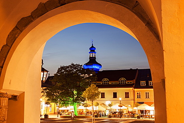 Illuminated Main Square with sidewalk cafe and blue onion dome seen through arch, Poland